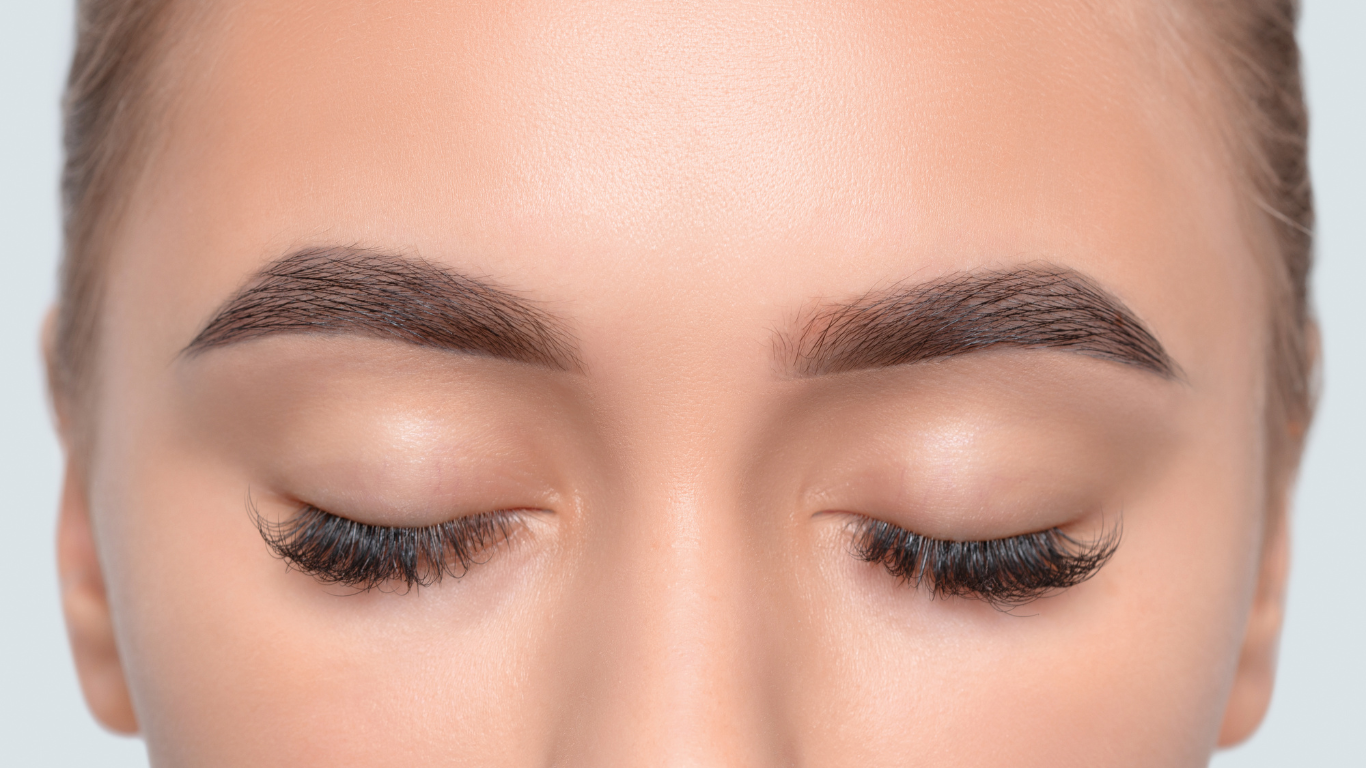 A close-up of a woman’s closed eyes showcasing perfectly shaped, defined eyebrows and long, full lashes. The skin appears smooth and flawless, reflecting the results of professional brow shaping and lash treatments available at Honeys Hair & Beauty in Taunton.