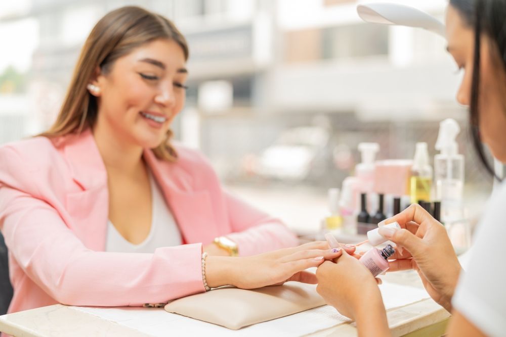 Smiling woman in pink blazer getting a manicure as nail technician applies polish
