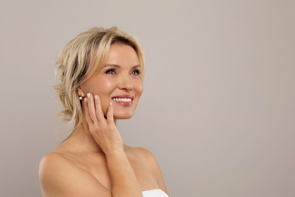Smiling woman touches cheek while looking up against neutral background