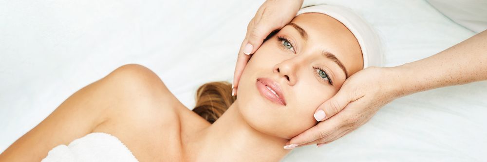 Spa therapist performs gentle facial massage on relaxed woman wearing headband